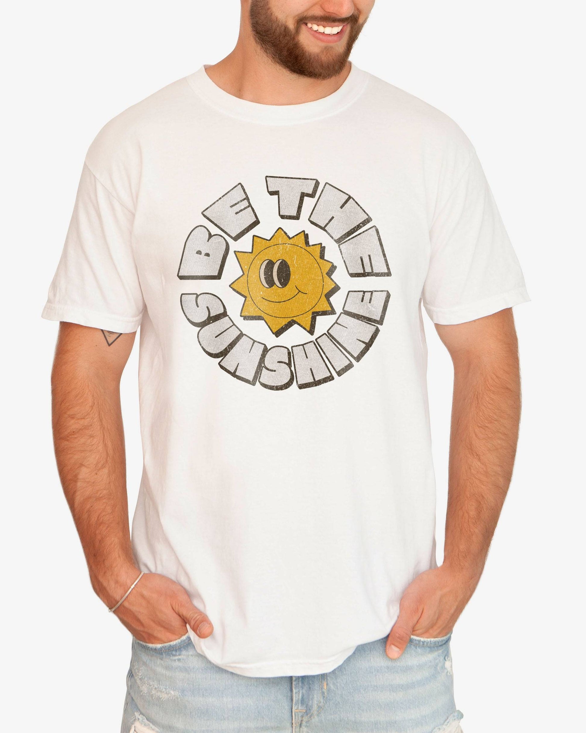 Man wearing a white Be The Sunshine shirt with a retro boho sun graphic.