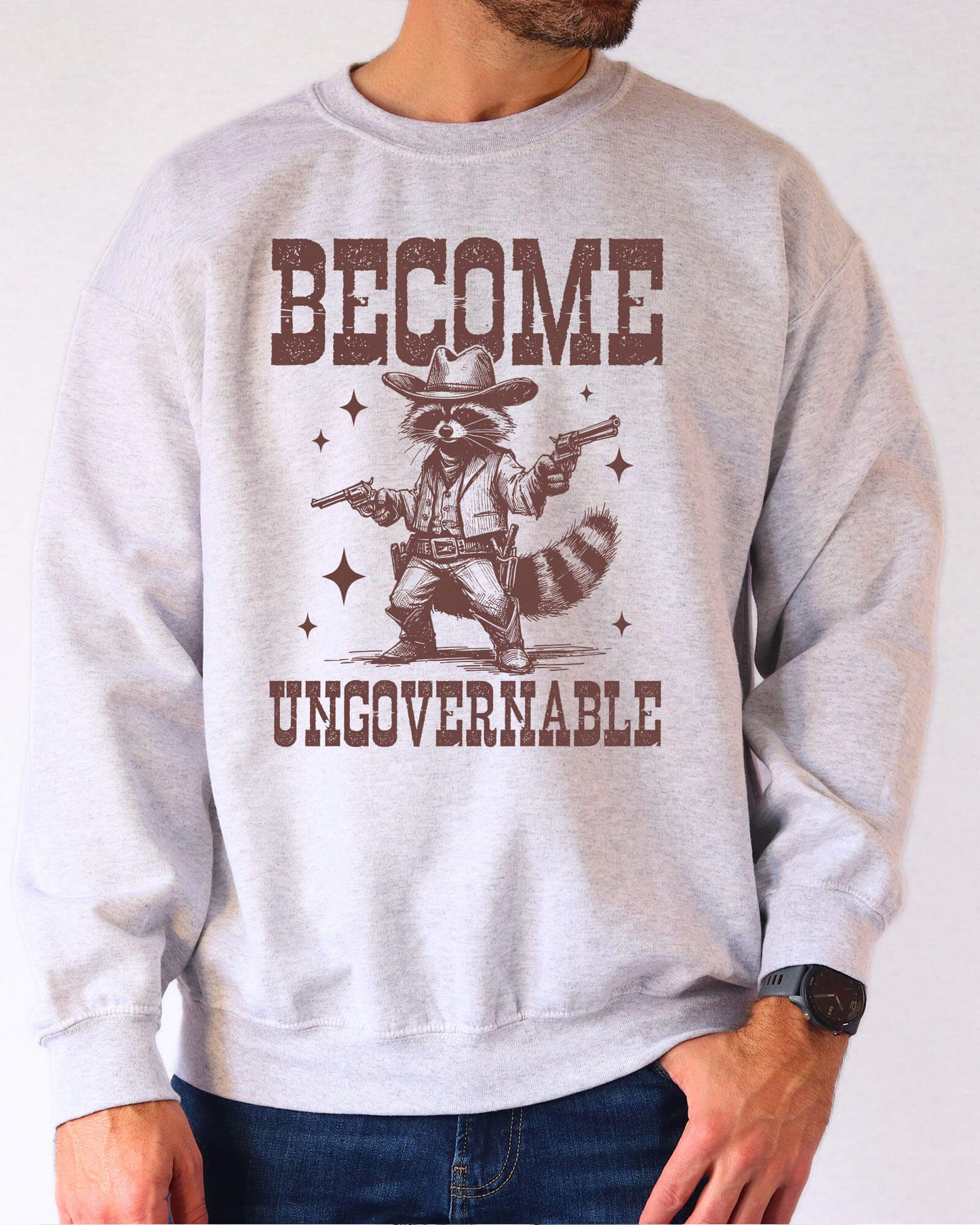 Man wearing an ash gray sweatshirt with a retro cowboy raccoon and the text “Become Ungovernable.”