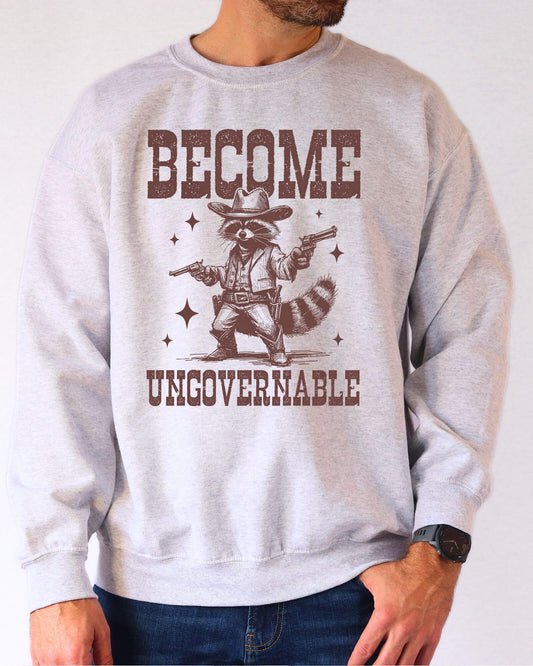 Man wearing an ash gray sweatshirt with a retro cowboy raccoon and the text “Become Ungovernable.”
