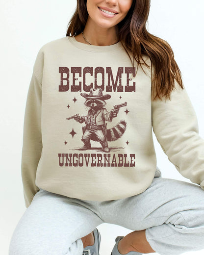 Woman wearing a sand beige sweatshirt with a retro cowboy raccoon and the text “Become Ungovernable.”