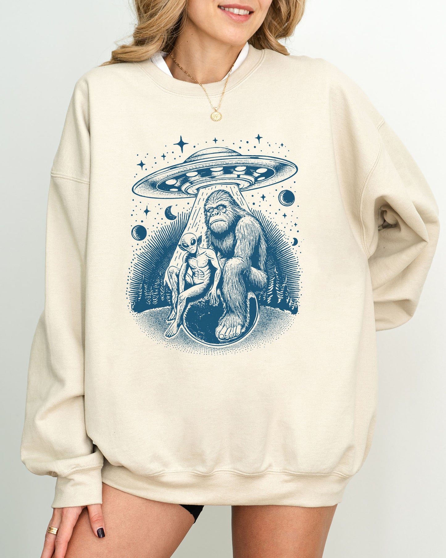 Model wearing sand color sweatshirt with 'Bigfoot, Alien And UFO' graphic design