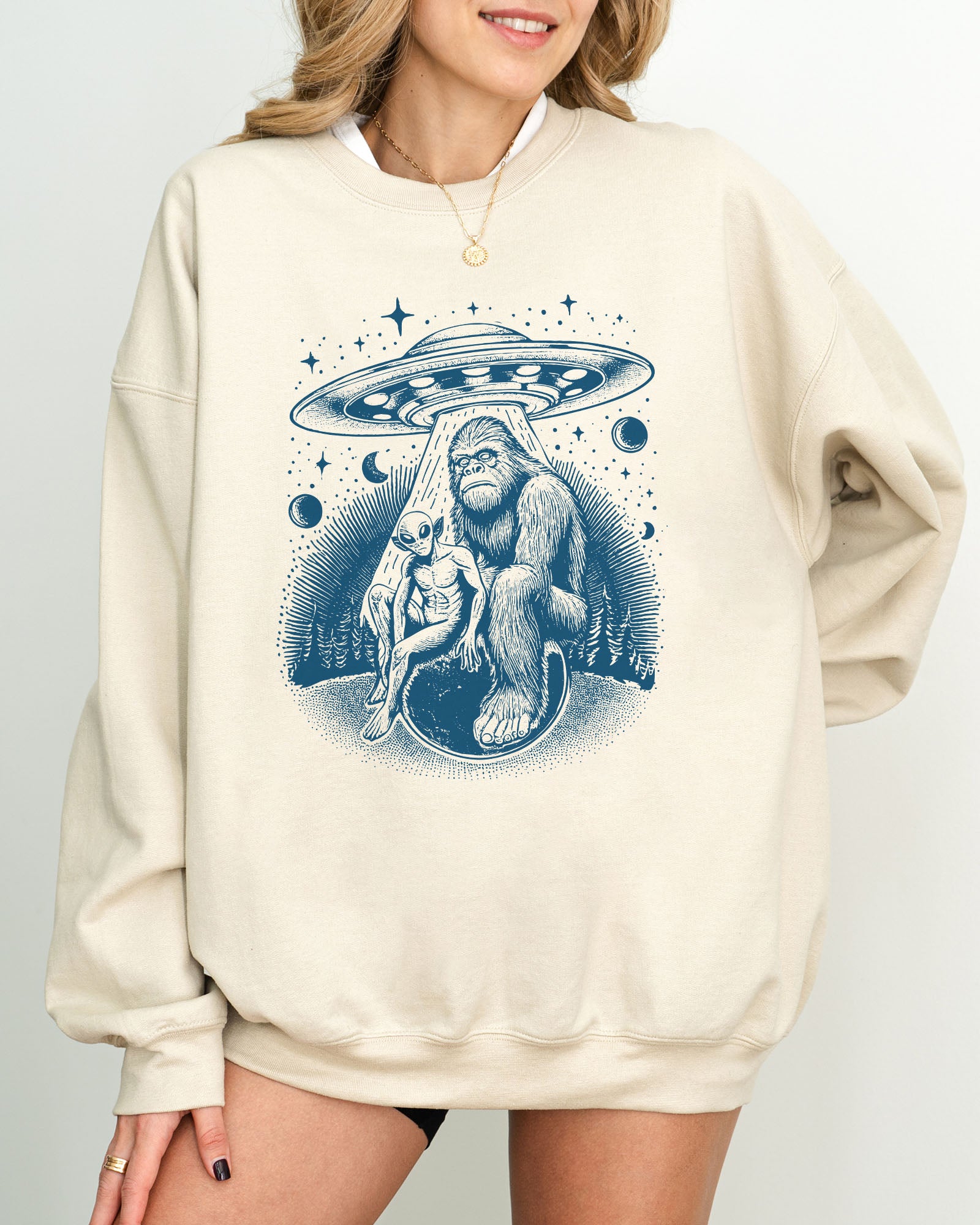 Model wearing sand color sweatshirt with 'Bigfoot, Alien And UFO' graphic design