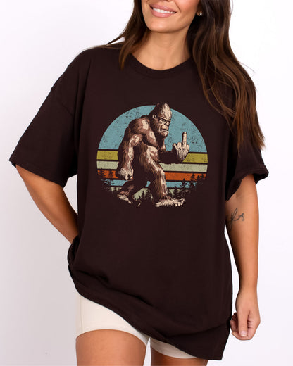 Model wearing dark chocolate color shirt with 'Bigfoot Showing Middle Finger' graphic design