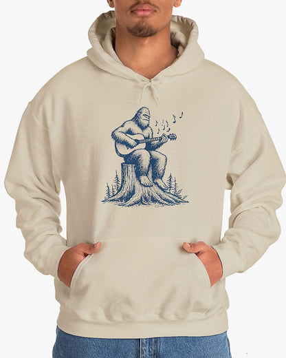 Man wearing sand beige hoodie with funny retro Bigfoot playing guitar graphic