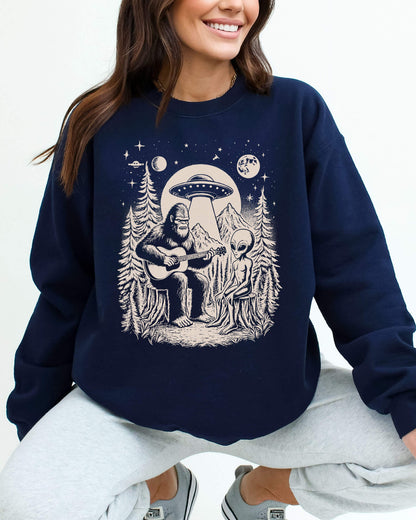 Woman wearing a navy blue sweatshirt featuring a retro graphic of Bigfoot playing guitar with an alien And UFO.