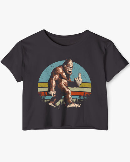 Flat lay of a black crop top with a funny retro-style Bigfoot flipping the middle finger graphic.