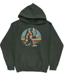 Flat lay of a forest green hoodie with a funny retro graphic of Bigfoot showing the middle finger.