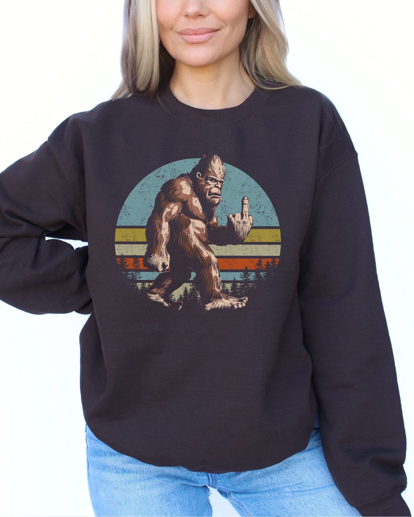 Woman wearing a dark chocolate color sweatshirt featuring a funny retro-style Bigfoot showing the middle finger graphic.