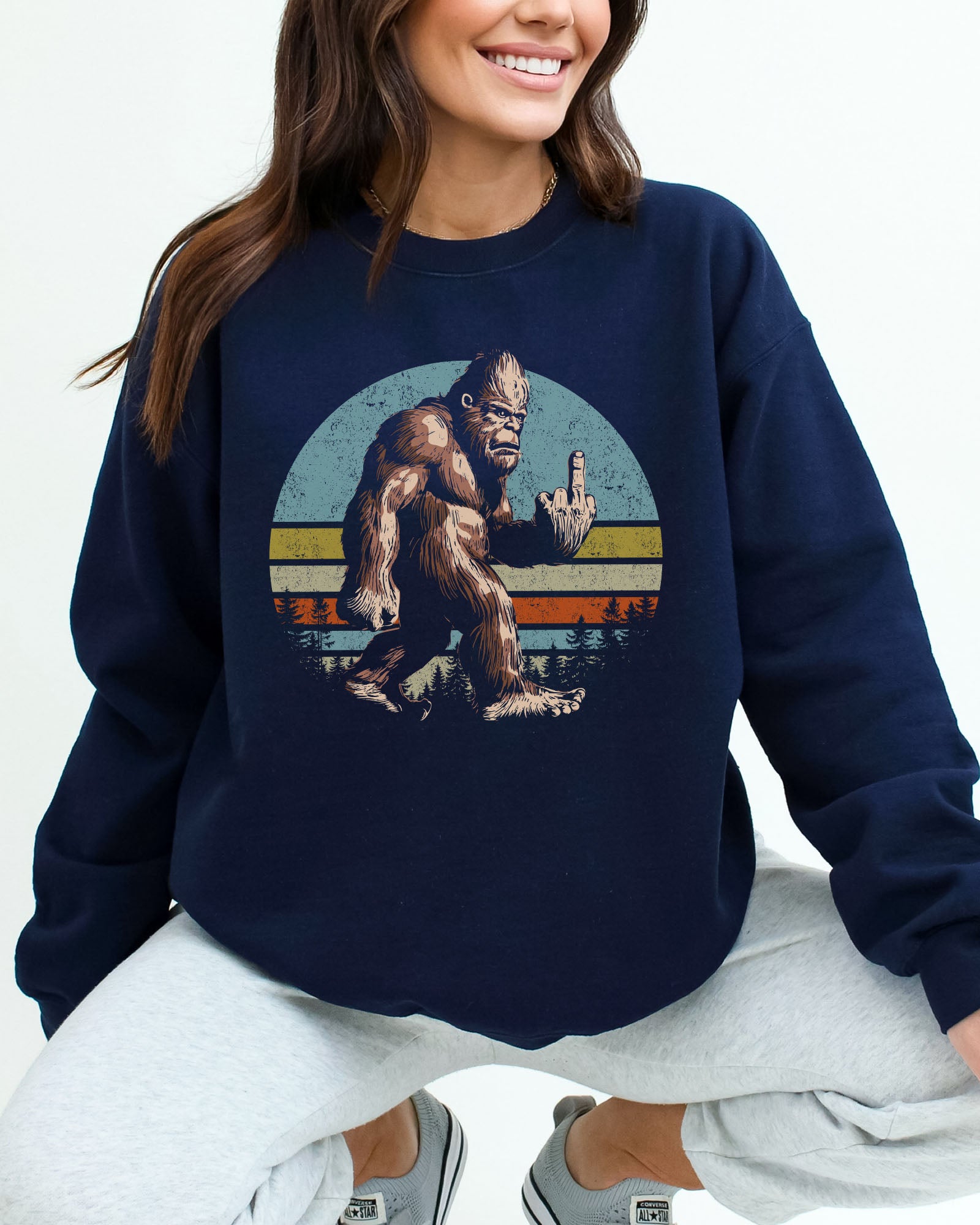 Woman wearing a navy blue sweatshirt featuring a funny retro-style Bigfoot showing the middle finger graphic.