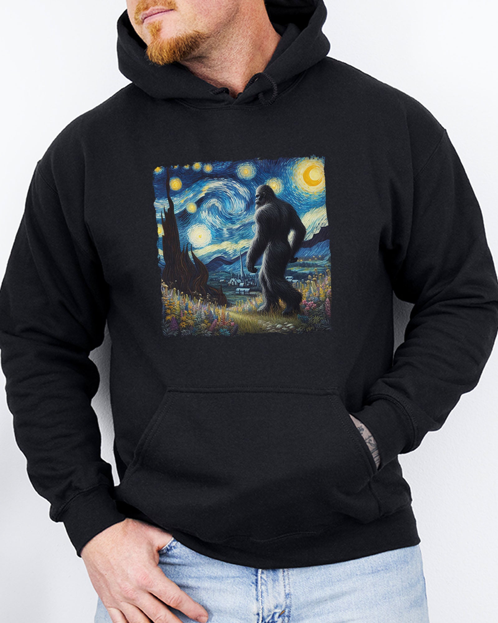 Man wearing a black hoodie featuring a Bigfoot walking through a starry night forest graphic.