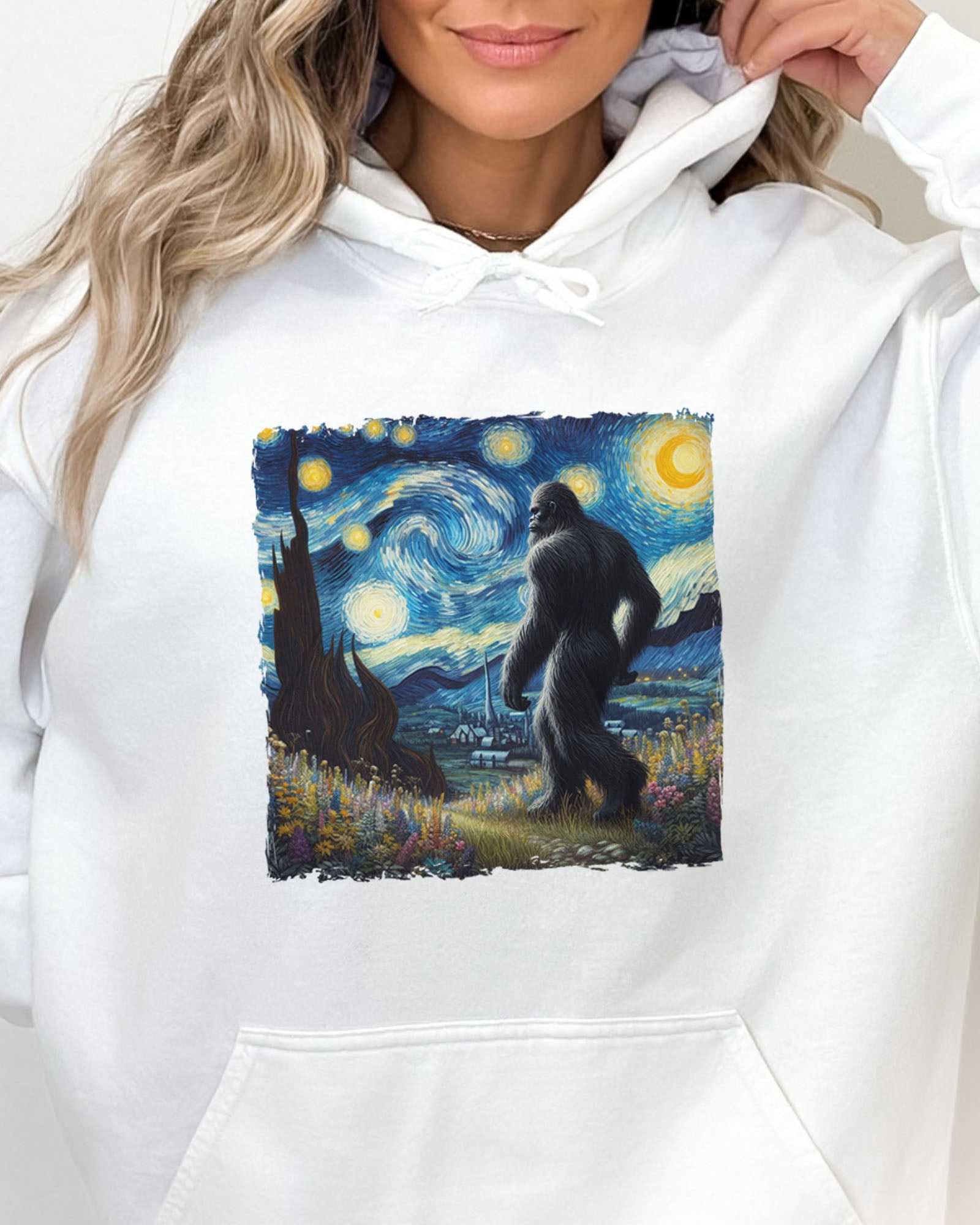 Close-up of a white hoodie featuring a Bigfoot walking through a starry night forest graphic.