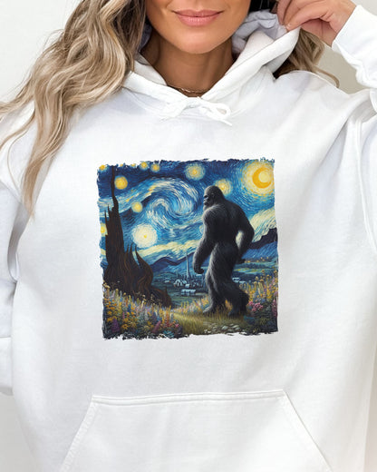 Close-up of a white hoodie featuring a Bigfoot walking through a starry night forest graphic.