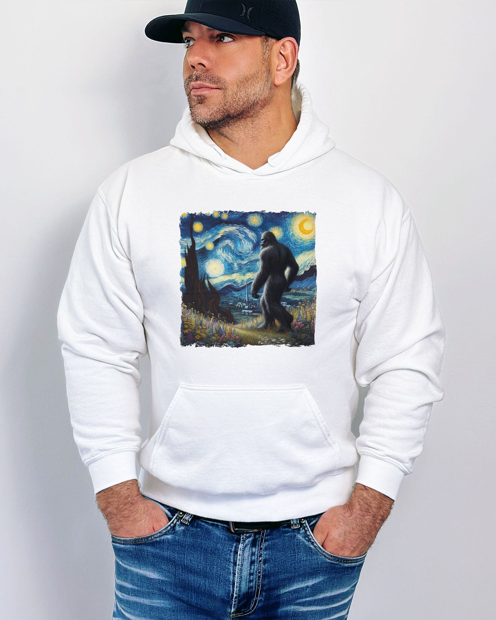 Man wearing a white hoodie featuring a Bigfoot walking through a starry night forest graphic.