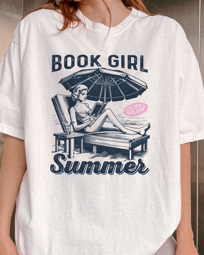 Close-up of woman wearing white "Book Girl Summer" shirt with retro graphic of a woman on a beach lounger reading a book.