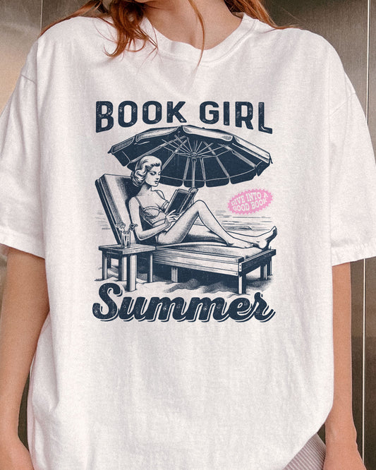 Close-up of woman wearing white "Book Girl Summer" shirt with retro graphic of a woman on a beach lounger reading a book.