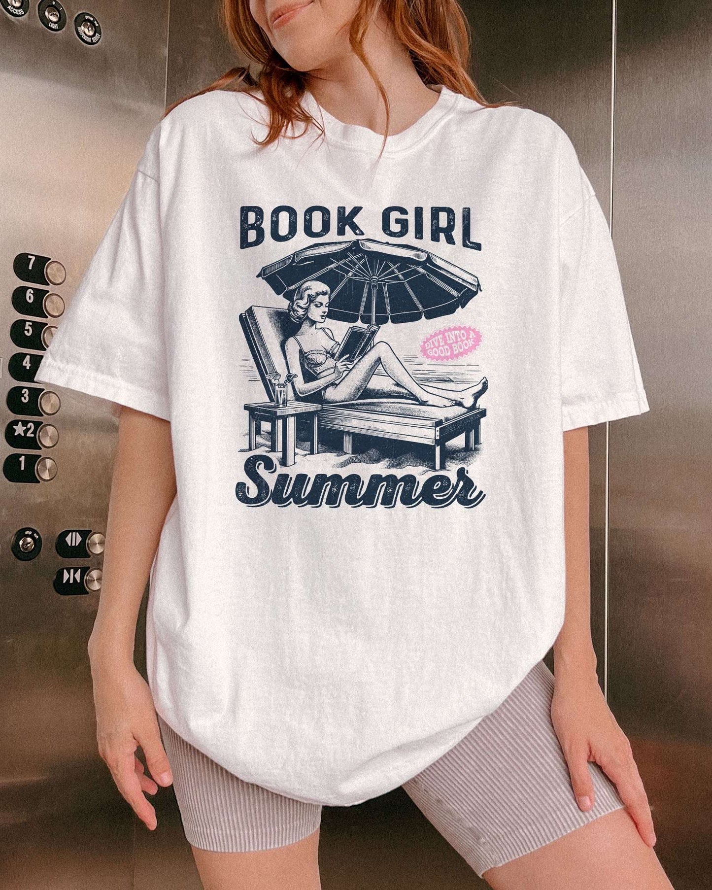 Woman wearing white "Book Girl Summer" shirt with retro graphic of a woman on a beach lounger reading a book.
