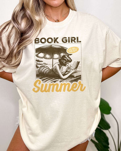 Woman wearing "Book Girl Summer" t-shirt in ivory color and with a retro graphic of a woman reading on a beach.