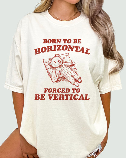 Woman modeling a natural beige 'Born To Be Horizontal, Forced To Be Vertical' unisex T-shirt with a funny retro bear graphic design, perfect for casual wear.