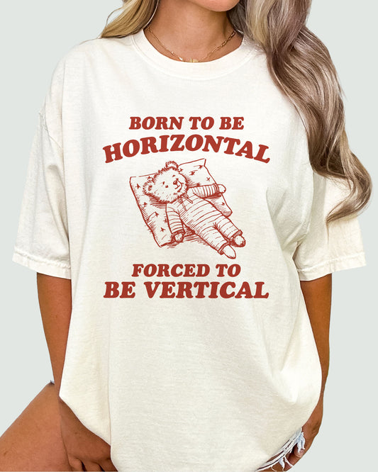 Woman modeling a natural beige 'Born To Be Horizontal, Forced To Be Vertical' unisex T-shirt with a funny retro bear graphic design, perfect for casual wear.