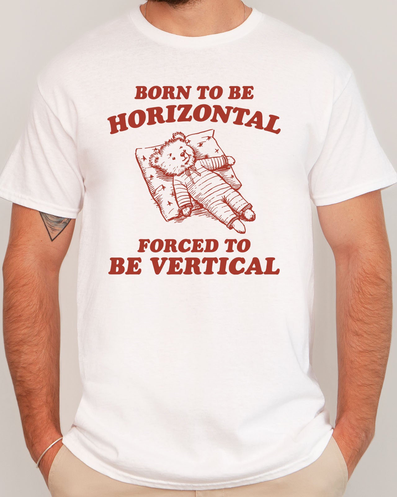 Man modeling a white 'Born To Be Horizontal, Forced To Be Vertical' unisex T-shirt with a funny retro bear graphic design, perfect for casual wear.