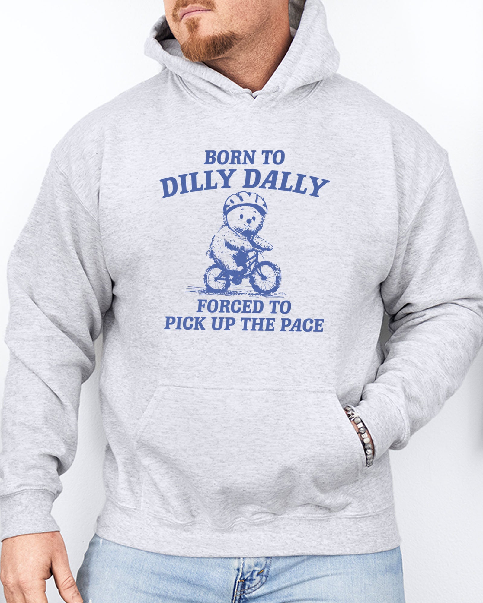 Man wearing an ash gray hoodie featuring a vintage-style bear riding a bike graphic with the quote 'Born To Dilly Dally, Forced To Pick Up The Pace'.