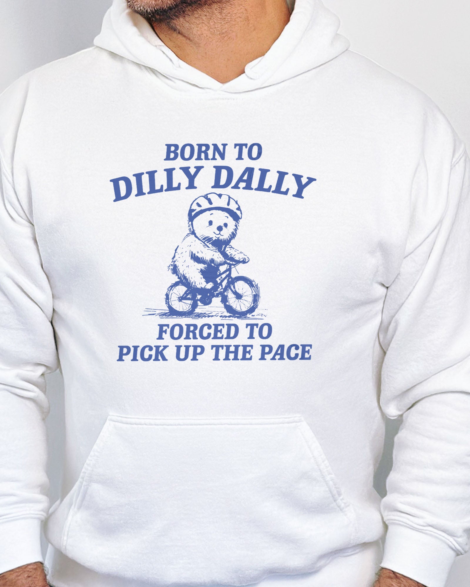 Close up of a white hoodie featuring a vintage-style bear riding a bike graphic with the quote 'Born To Dilly Dally, Forced To Pick Up The Pace'.
