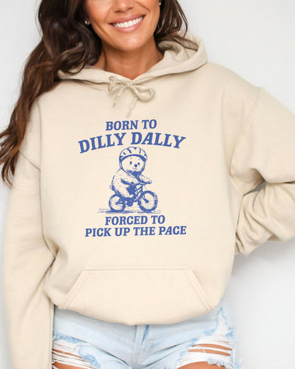 Woman wearing a sand beige hoodie featuring a vintage-style bear riding a bike graphic with the quote 'Born To Dilly Dally, Forced To Pick Up The Pace'.