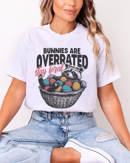 Model wearing ash color shirt with 'Bunnies Are Overrated - Stay Feral' easter raccoon graphic design