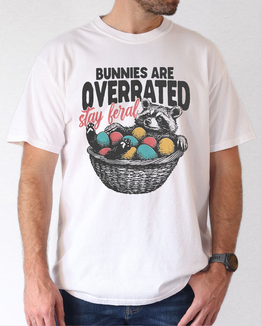 Model wearing white color shirt with 'Bunnies Are Overrated - Stay Feral' easter raccoon graphic design