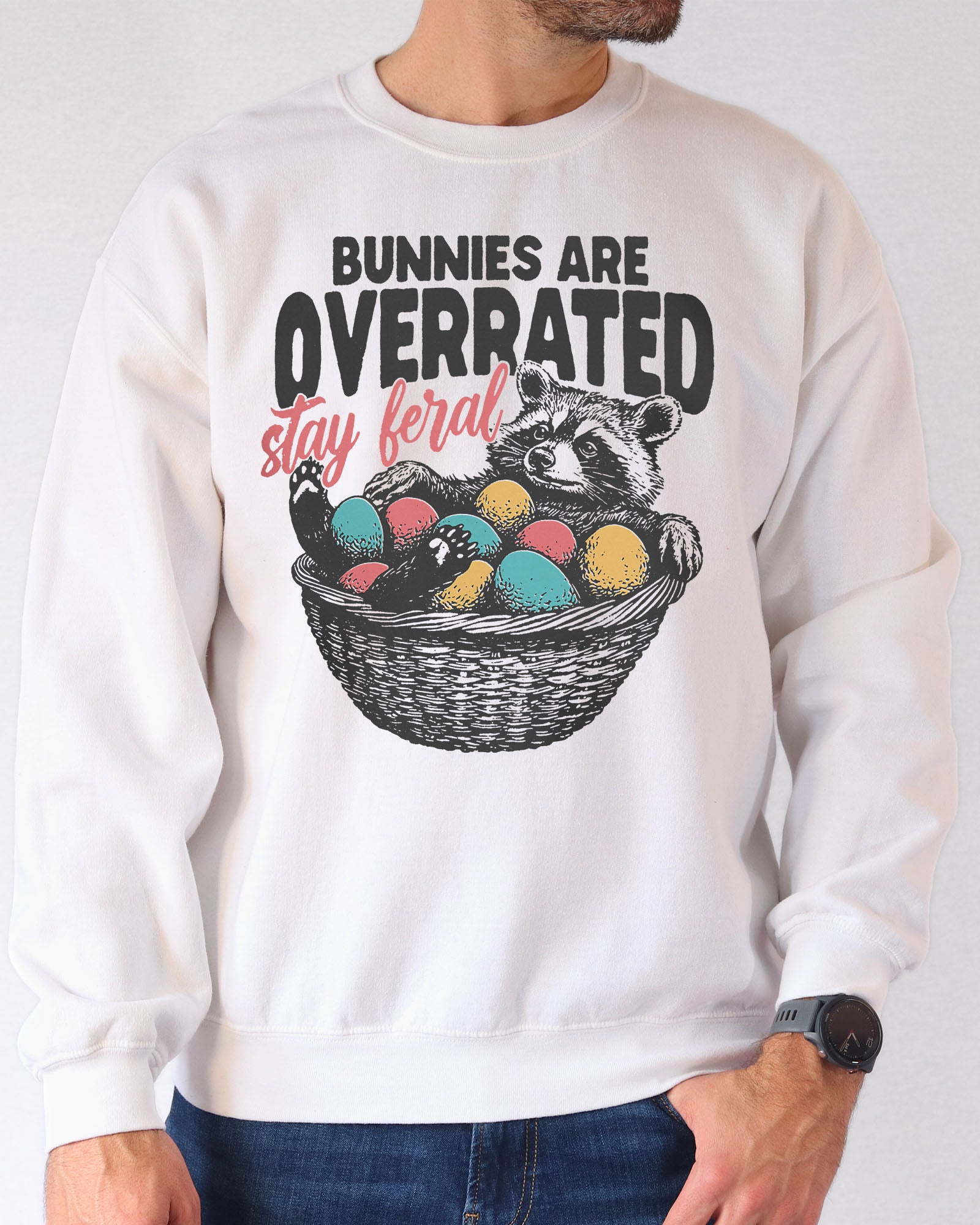 Man wearing a white sweatshirt with a funny retro-style graphic of a raccoon in an Easter egg basket and the quote "Bunnies Are Overrated, Stay Feral".