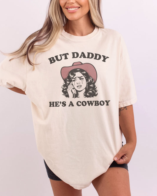 Woman wearing an ivory "But Daddy He's a Cowboy" shirt with a funny retro graphic of a cowgirl crying while talking on the phone.