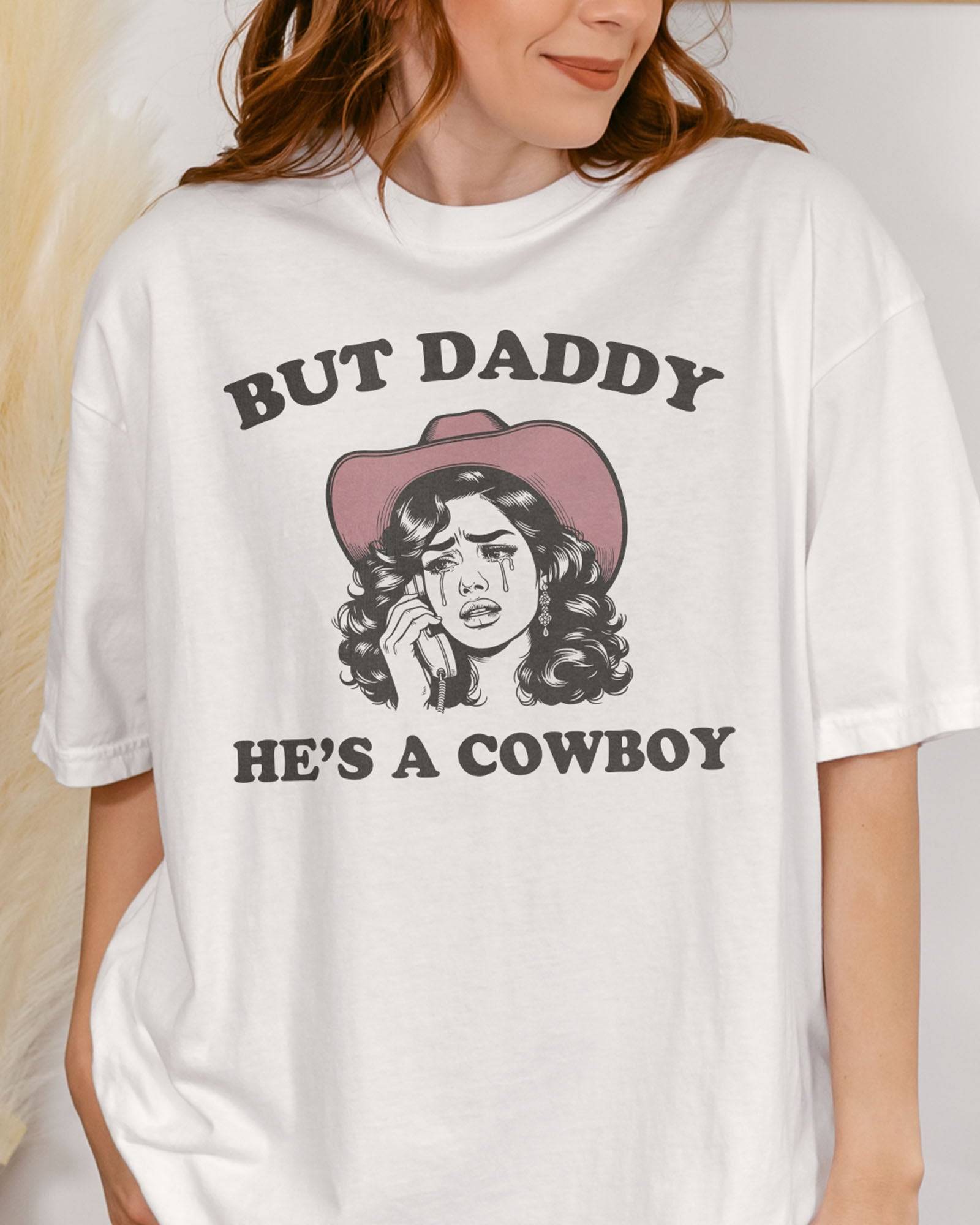 Close-up of woman wearing a white "But Daddy He's a Cowboy" shirt with a funny retro graphic of a cowgirl crying while talking on the phone.