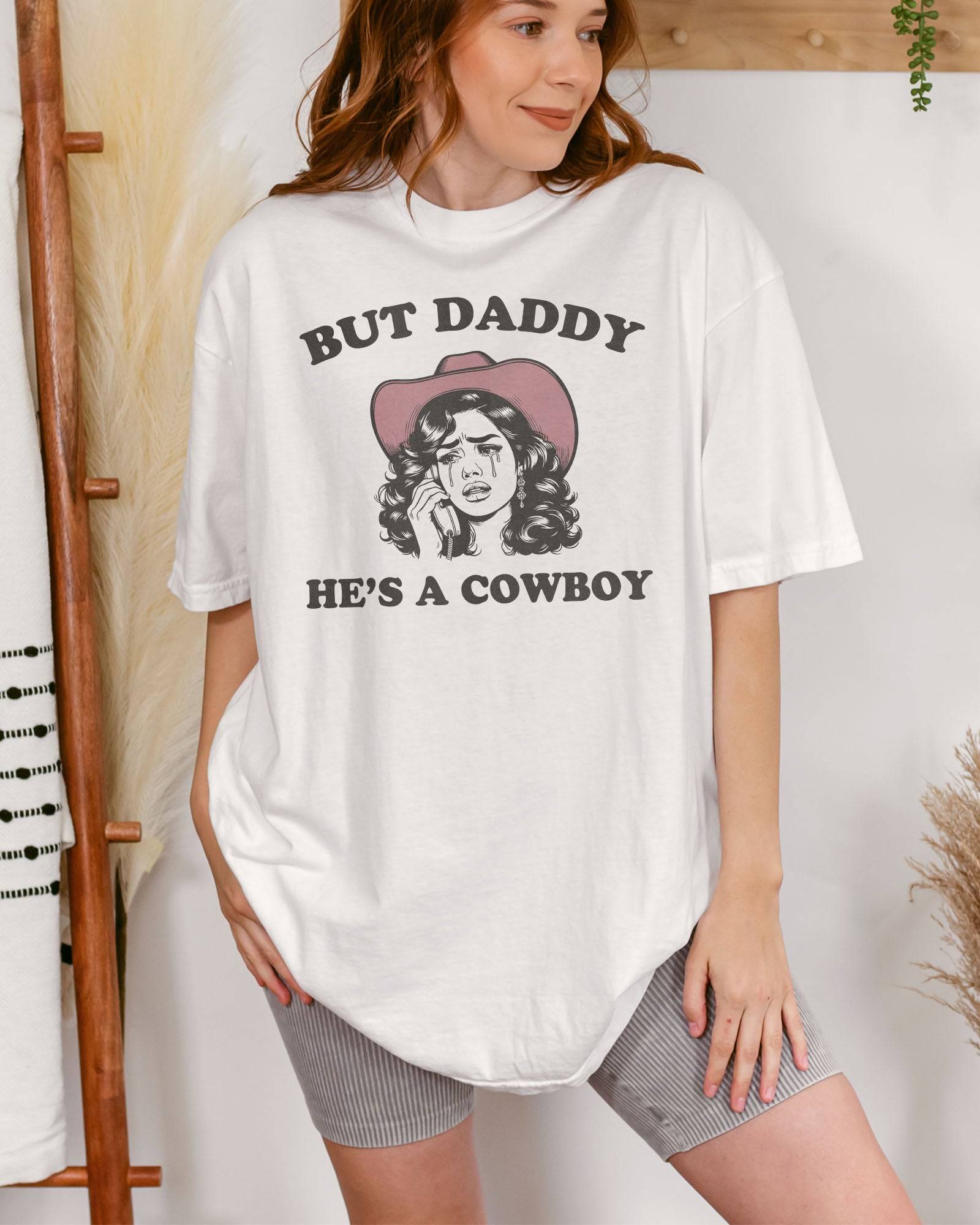 Woman wearing a white "But Daddy He's a Cowboy" shirt with a funny retro graphic of a cowgirl crying while talking on the phone.