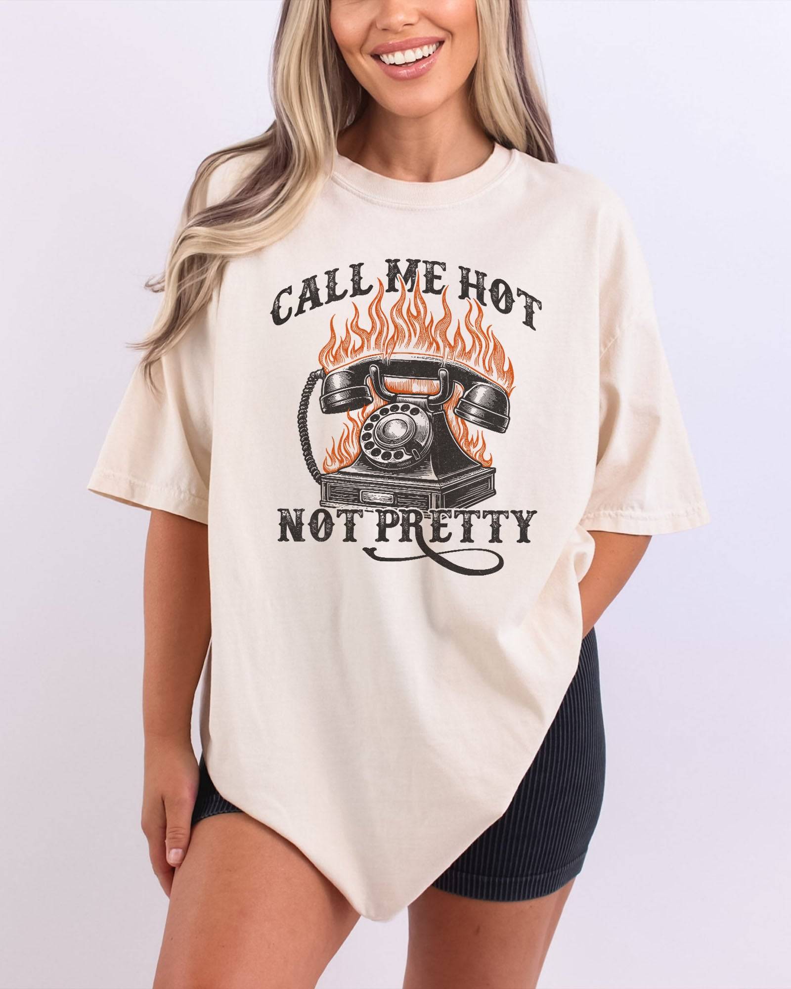 Woman wearing an ivory 'Call Me Hot Not Pretty' shirt with a retro graphic of a burning phone.