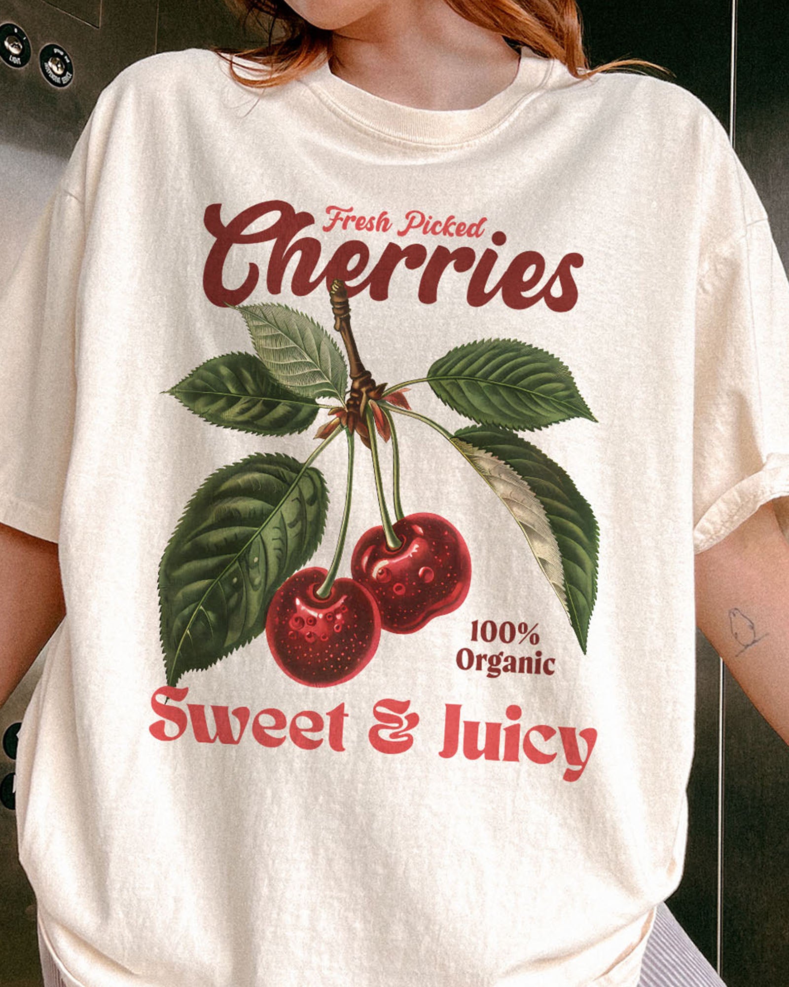 Close-up of woman wearing an ivory "Cherries - Sweet & Juicy" shirt with a retro cherry graphic.