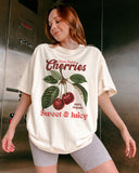 Woman wearing an ivory "Cherries - Sweet & Juicy" shirt with a retro cherry graphic.