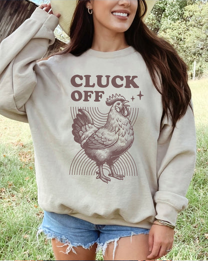 Model wearing sand color sweatshirt with 'Cluck Off' graphic design