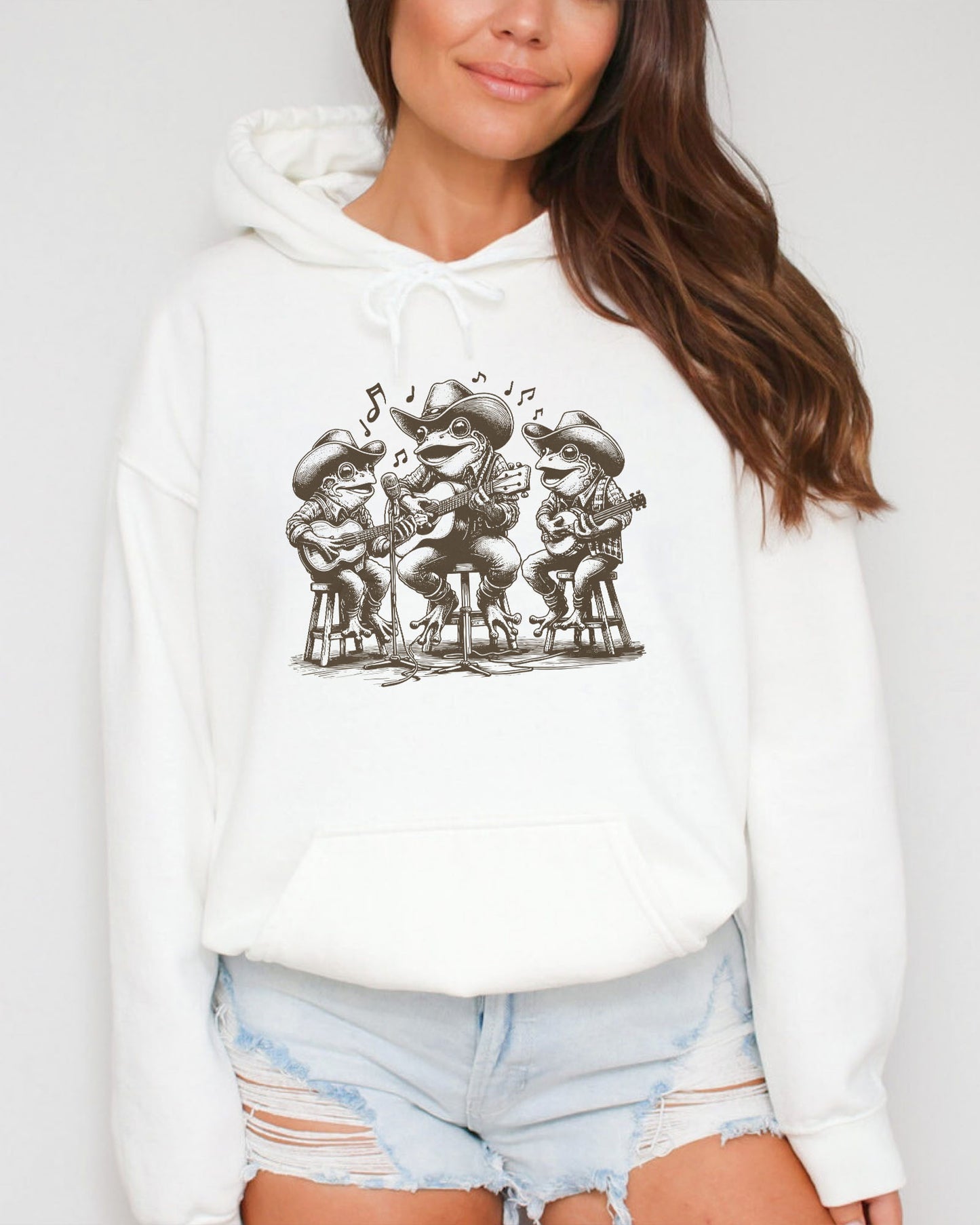 Woman wearing white-colored hoodie featuring a funny retro country frog band graphic.