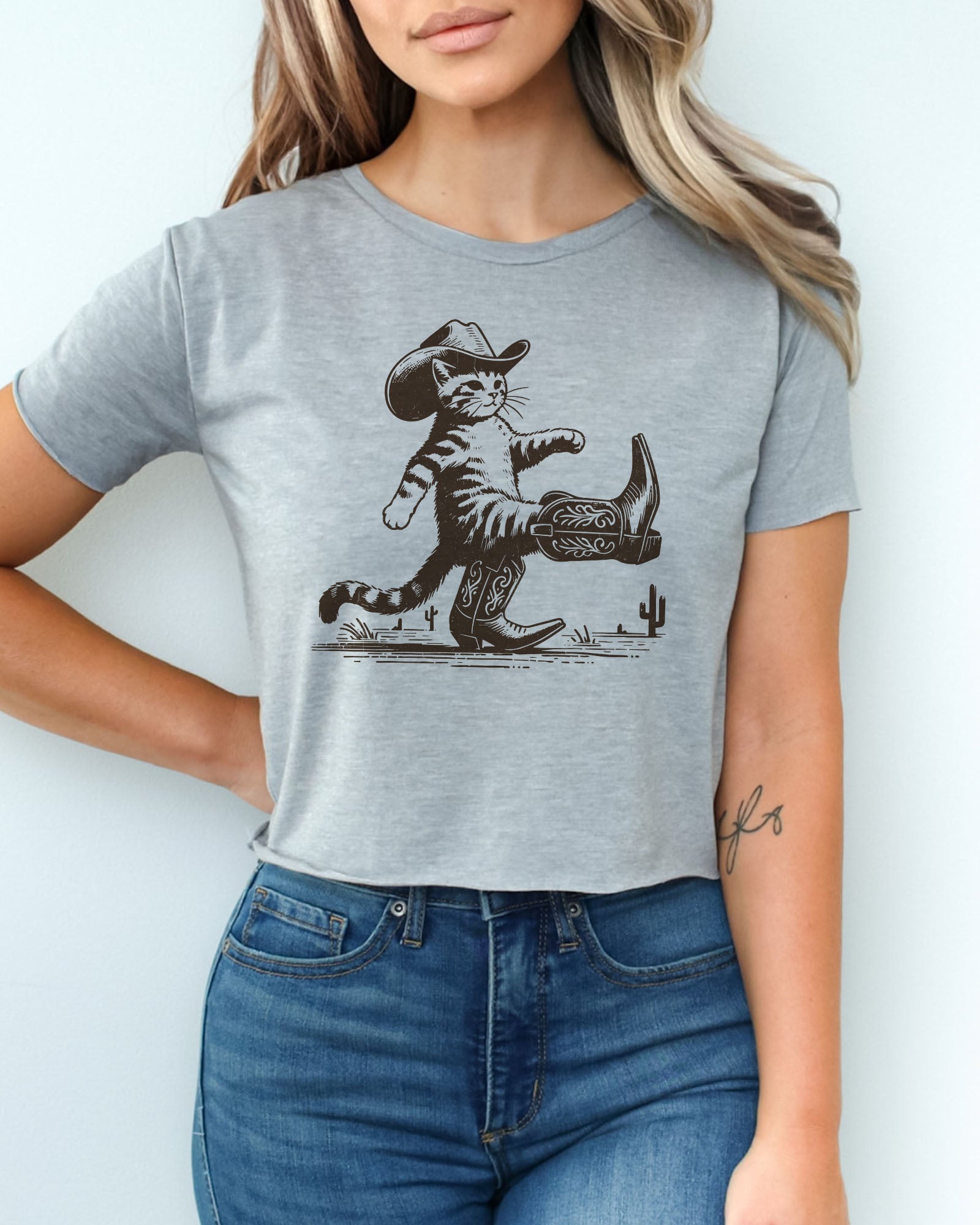 Woman wearing heather gray crop top featuring a funny retro cowboy cat graphic.