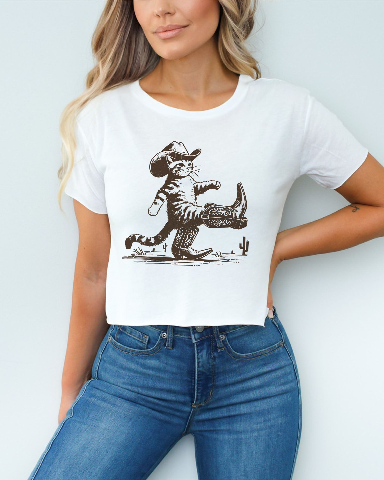 Woman wearing white crop top featuring a funny retro cowboy cat graphic.