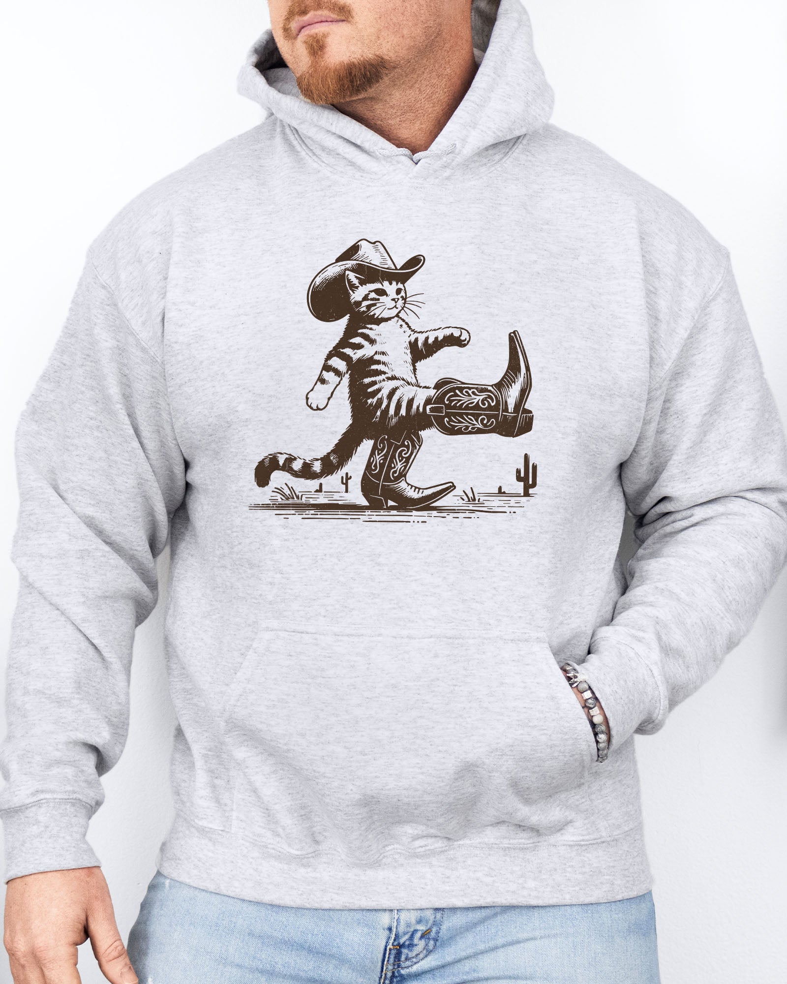 Man wearing an ash gray hoodie featuring a retro-style cowboy cat graphic with a funny Western theme.
