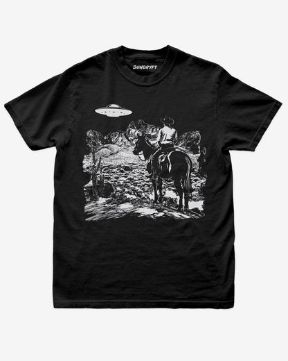 Black “Cowboy UFO” shirt with cowboy riding horse through desert under UFO graphic flat lay.