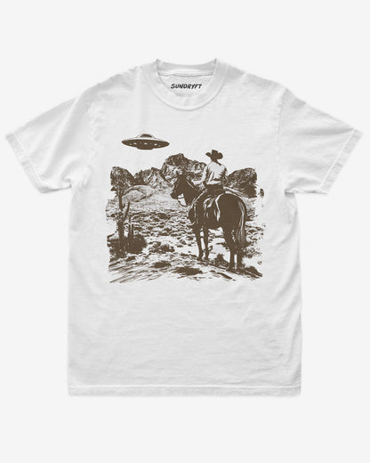 White “Cowboy UFO” shirt with cowboy riding horse through desert under UFO graphic flat lay.