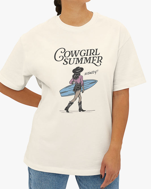 Woman wearing a natural beige 'Cowgirl Summer' shirt featuring a retro cowgirl graphic holding a surfboard.