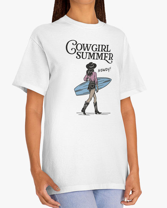 Woman wearing a white 'Cowgirl Summer' shirt featuring a retro cowgirl graphic holding a surfboard.