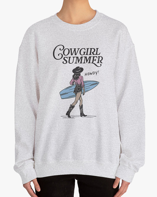 Woman wearing an ash gray 'Cowgirl Summer' sweatshirt featuring a retro graphic of a cowgirl holding a surfboard.