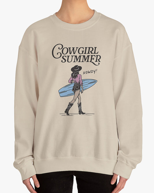 Woman wearing a sand beige 'Cowgirl Summer' sweatshirt featuring a retro graphic of a cowgirl holding a surfboard.