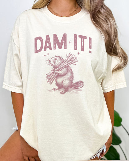 Woman wearing funny retro beaver graphic shirt in natural beige color with the quote "Dam It"