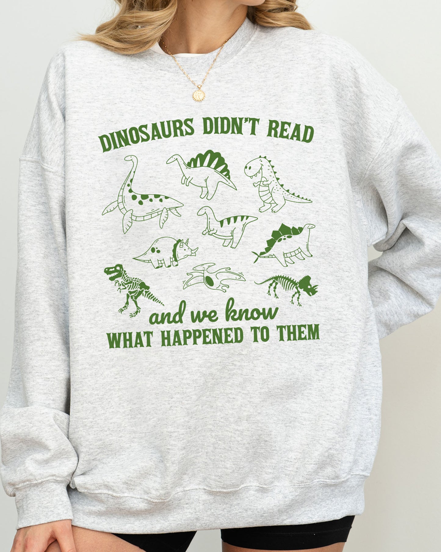 Close-up of model wearing ash color sweatshirt with 'Dinosaurs Didn't Read And We Know What Happened To Them' graphic design