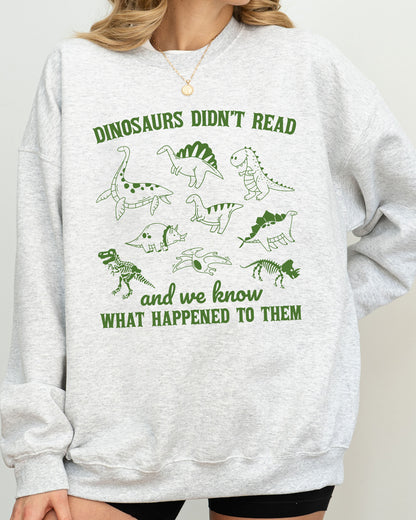 Close-up of model wearing ash color sweatshirt with 'Dinosaurs Didn't Read And We Know What Happened To Them' graphic design